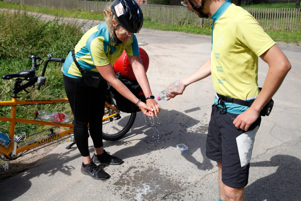 MUT-TOUR: Sucht_Selbstfürsorge MUT-TOUR-Teilnehmer hält eine Wasserflasche, damit sich Michaela die Hände waschen kann