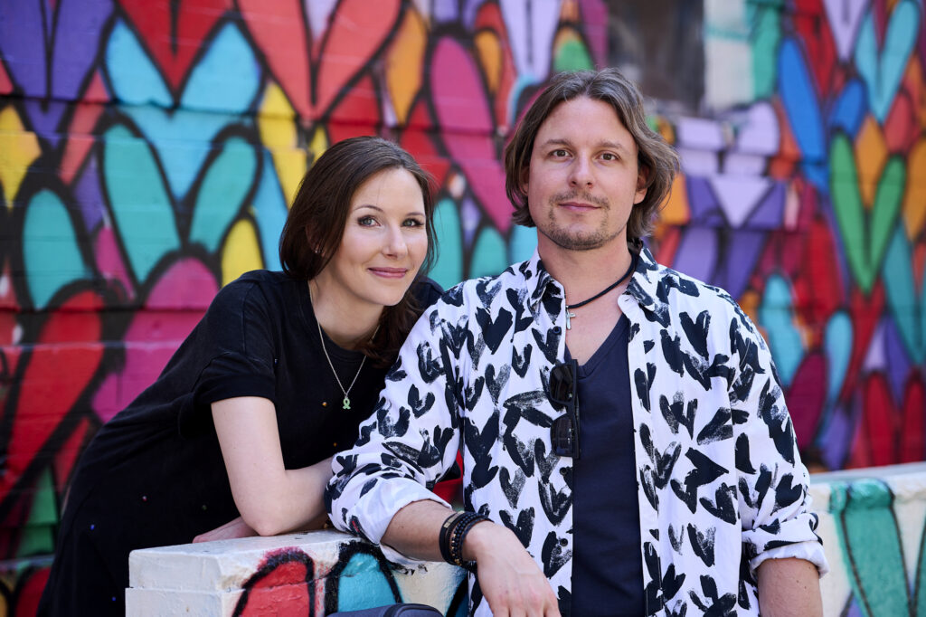 ME and THE LION im Interview mit der MUT-TOUR Ani und Leo stehen nebeneinander, hinter ihnen einen bunt bemalte Wand