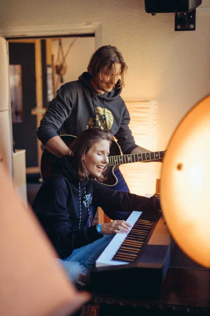 ME and THE LION_Musik_Interview Ani sitz am Klavier, hinter ihr steht Leo mit der Gitarre in der Hand