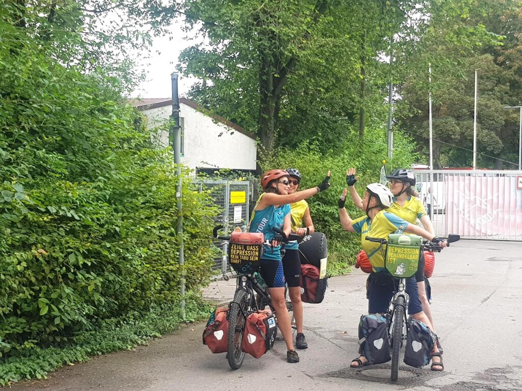 MUT-TOUR 2024_Tandem_Team_Unterstützung Vier MUT-TOUR-Teilnehmende auf zwei Tandems, die nebeneinander stehen und sich abklatschen